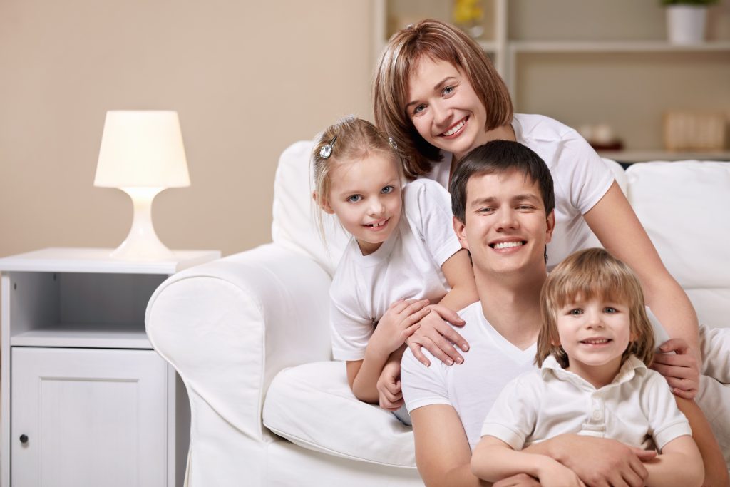 Happy family portrait on a white sofa, showcasing a clean and healthy home environment, that benefits from effective Air Cleaning Systems.